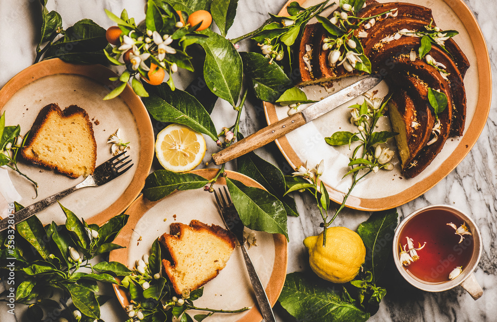 Flat-lay of homemade freshly baked Lemon cake, citrus tree blossom branches and black tea over white