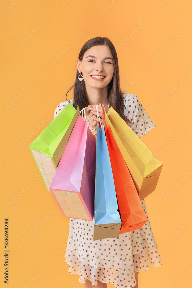 Beautiful young woman with shopping bags on color background