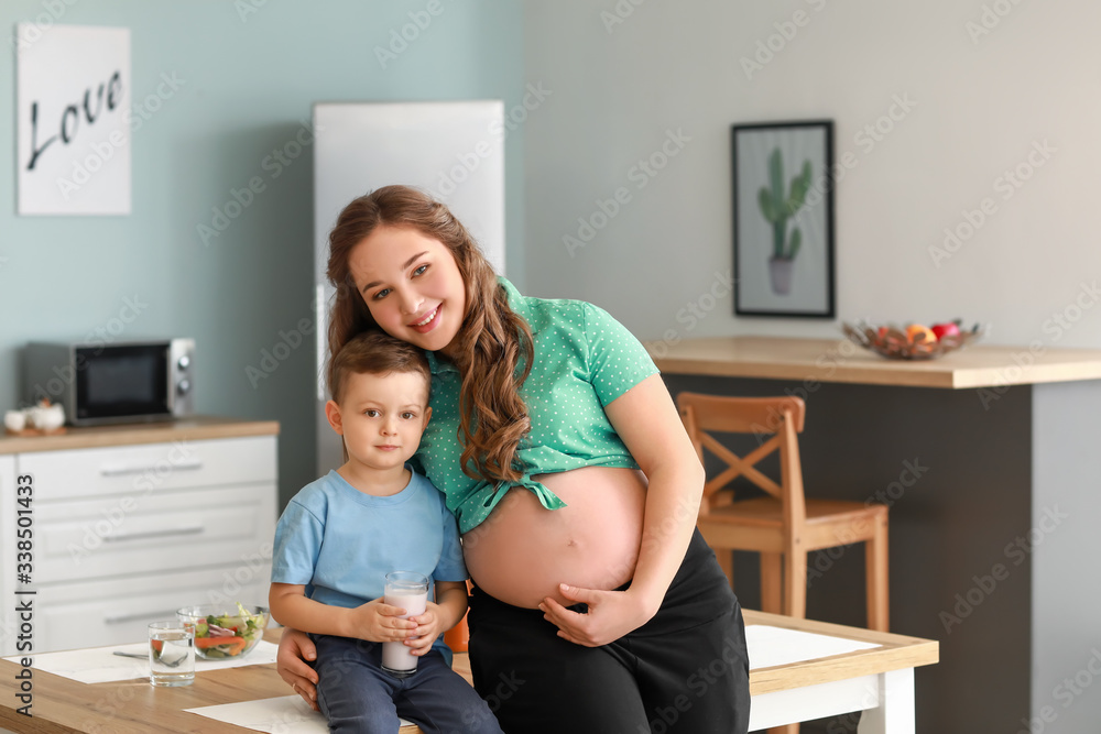 Beautiful pregnant woman and her little son in kitchen