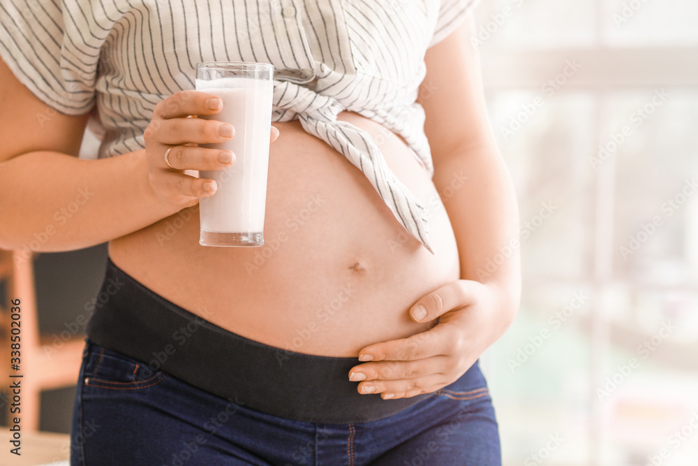 Beautiful pregnant woman with yogurt in kitchen, closeup