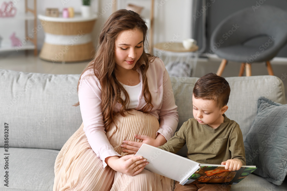 Beautiful pregnant woman with her little son reading book at home