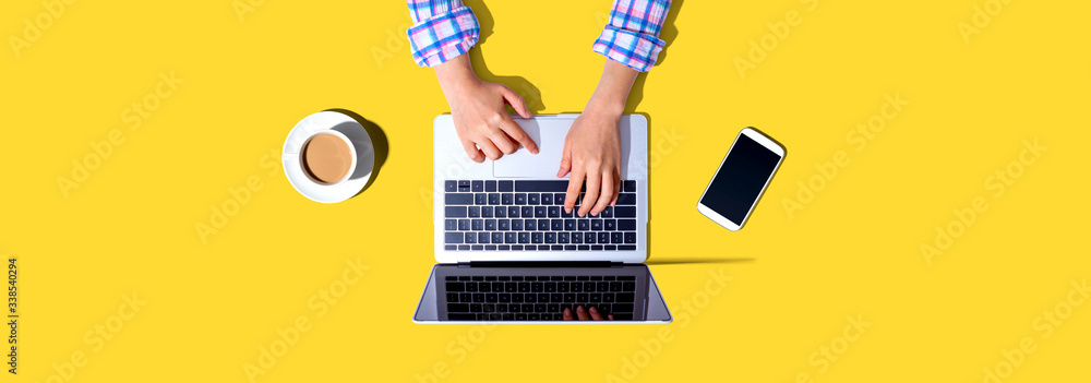 Woman using a laptop computer with a phone and a cup of coffee