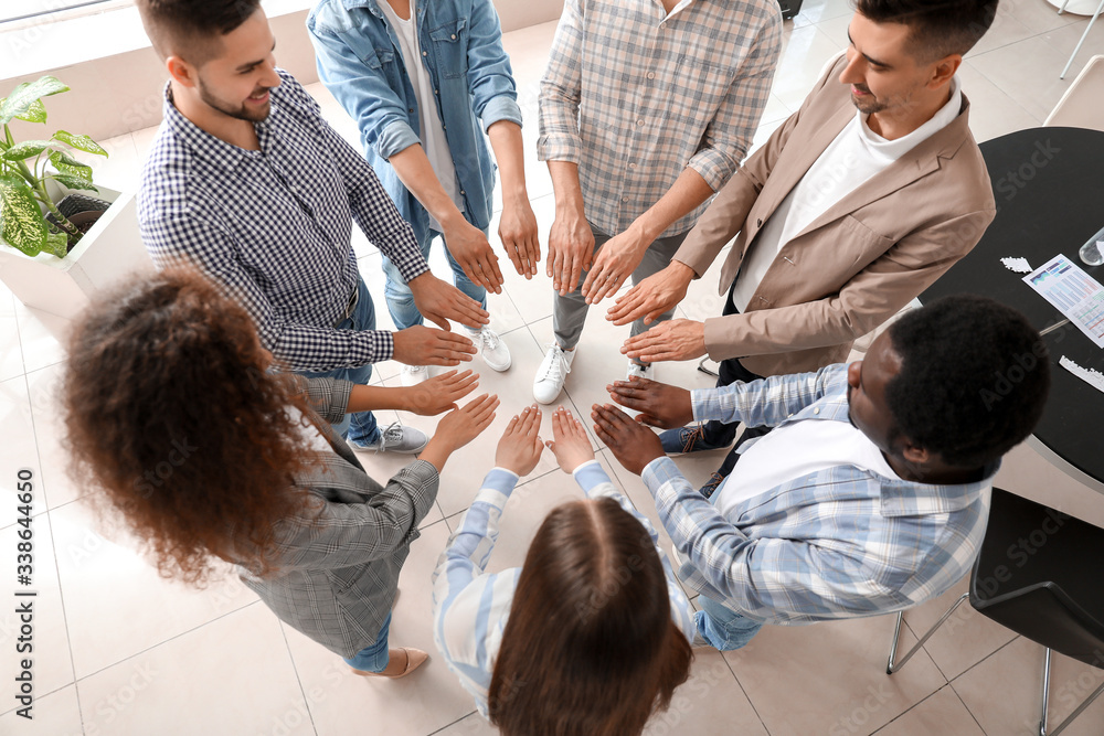 Group of people putting hands together indoors, top view. Unity concept