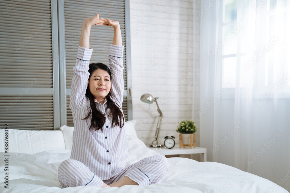 有魅力的年轻亚洲日本女性，醒来后坐在舒适的床上伸展身体放松我