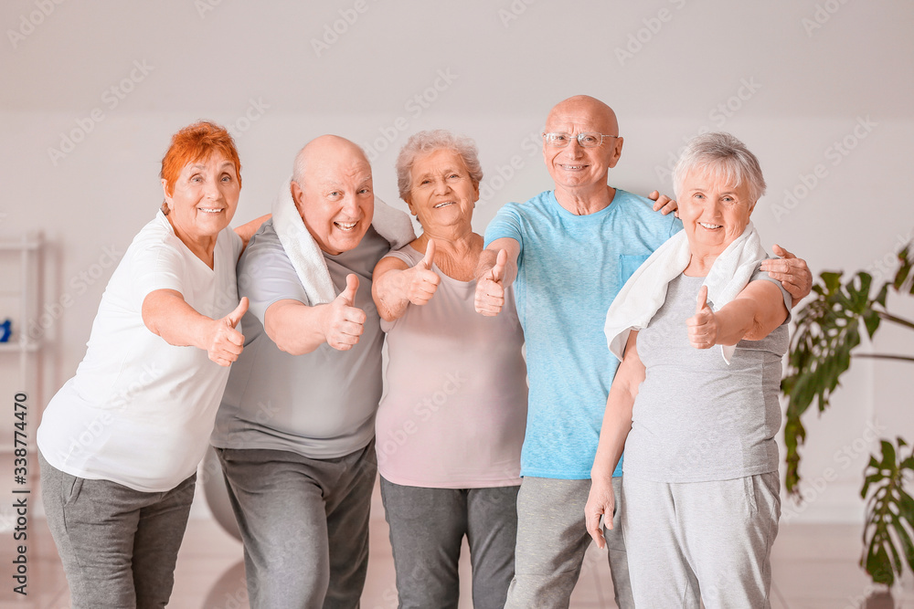 Happy elderly people showing thumb-up gesture in gym