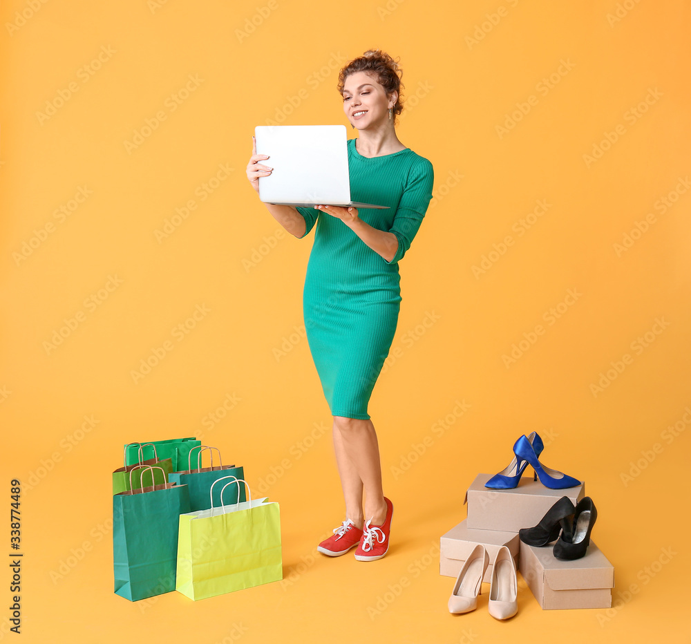 Young woman with laptop and shopping bags on color background