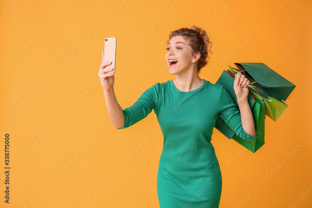 Beautiful young woman with mobile phone and shopping bags on color background