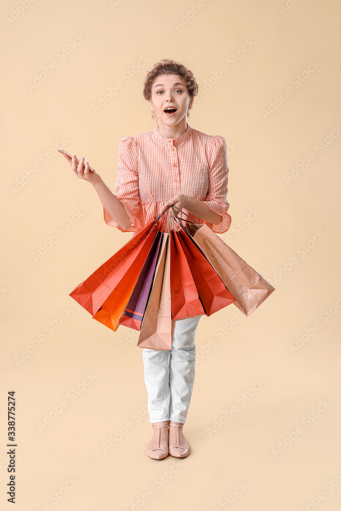 Surprised young woman with mobile phone and shopping bags on color background