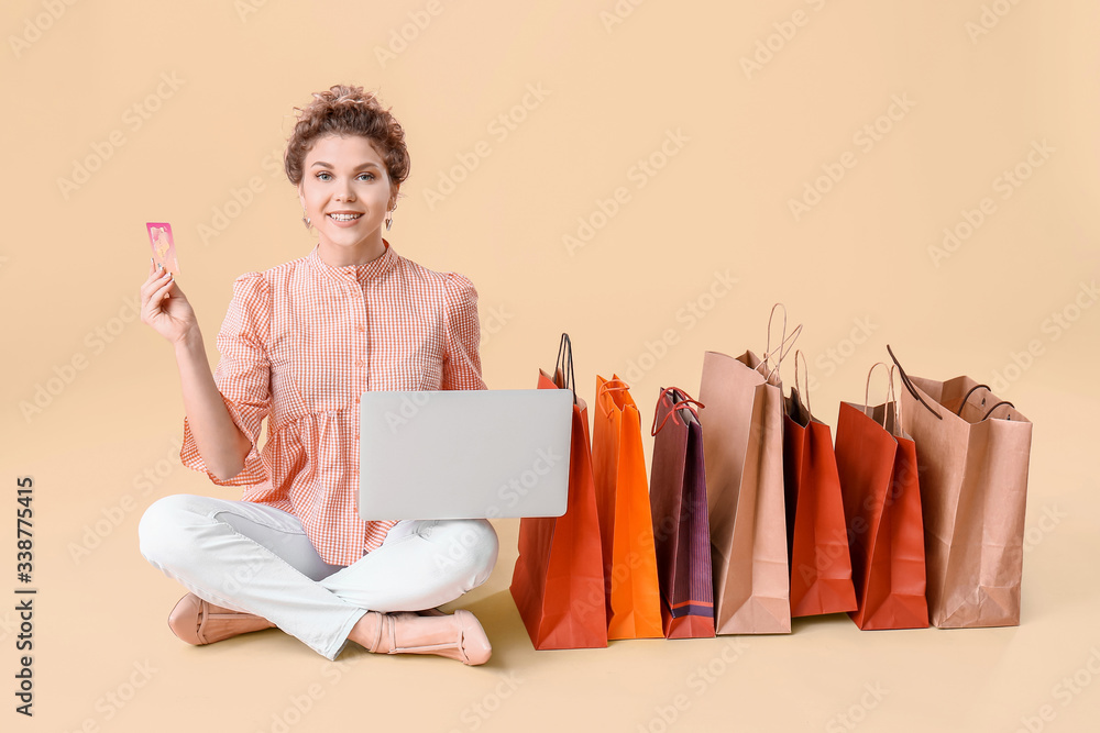 Beautiful young woman with laptop, credit card and shopping bags on color background