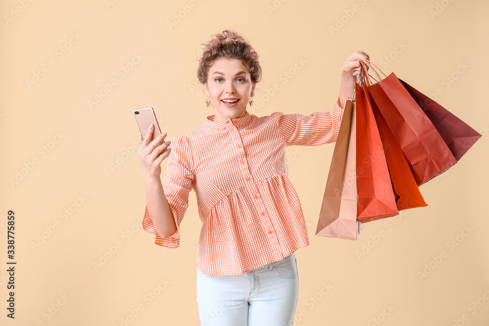 Beautiful young woman with mobile phone and shopping bags on color background