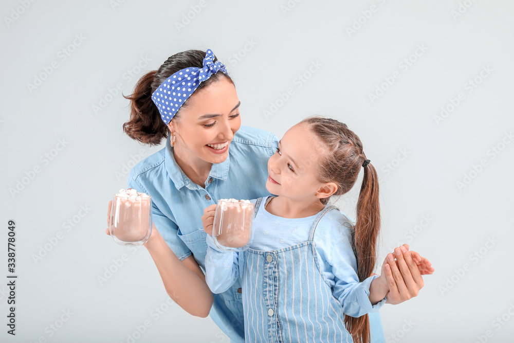 Woman and her little daughter with tasty cocoa drink on light background