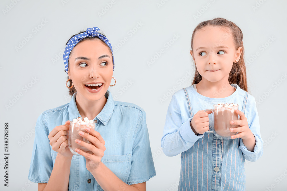 Woman and her little daughter with tasty cocoa drink on light background