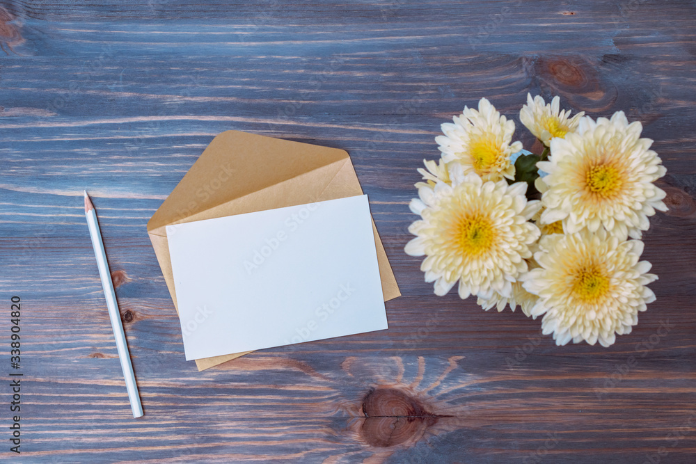 Mockup white wedding invitation and envelope with flowers in a vase on a wooden background