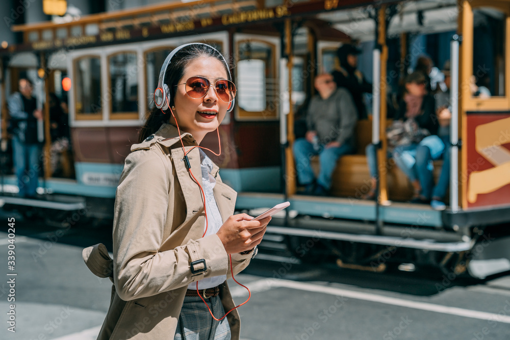 young beautiful asian chinese woman commuter in city street with headphones listening to music from 