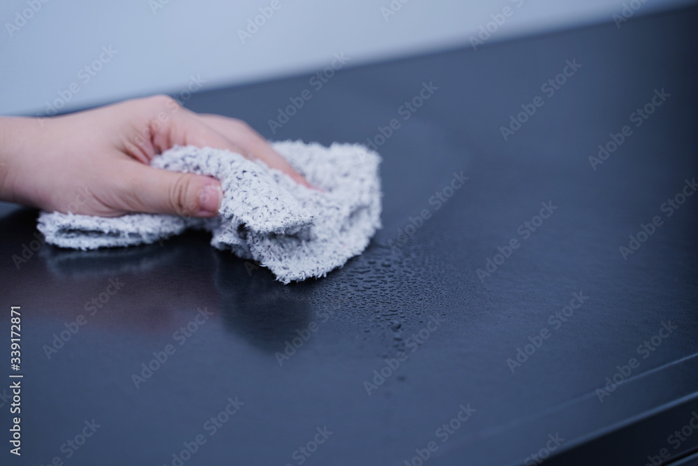 Young woman is holding spray bottle, rag to clean, wipe down office metal cabinet shelf accommodatio