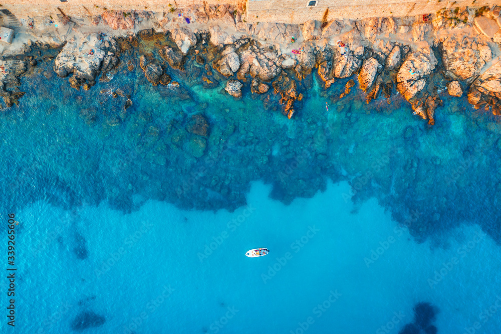 Aerial view of beach with stones and rocks, alone boat in adriatic sea at sunset in summer. Top view