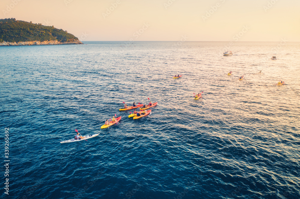 Aerial view of the people in kayaks in the sea at sunset in summer. Top view of floating canoe. Land