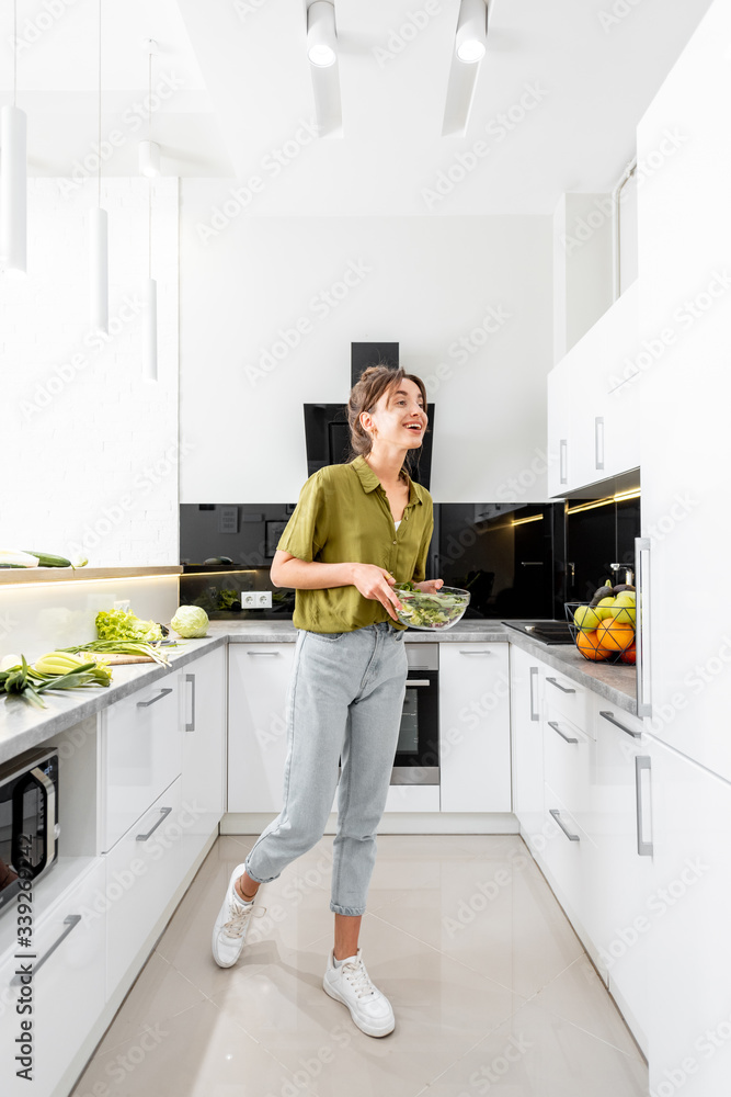 Woman cooking healthy food on the modern kitchen at home, wide interior view. Woman is motion blurre