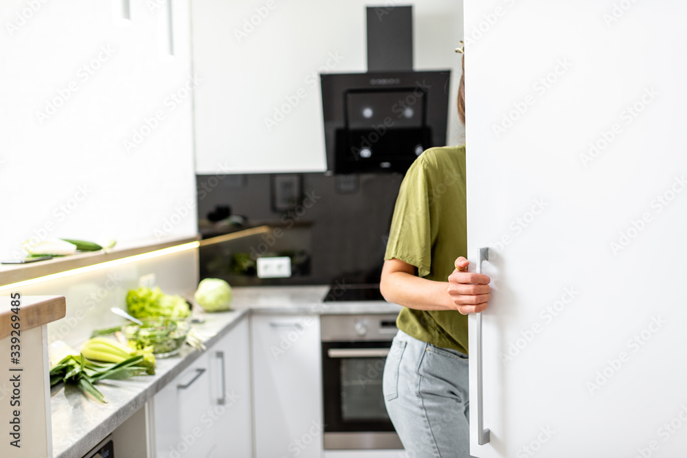 女人在家里的现代厨房里烹饪健康食品时看着冰箱