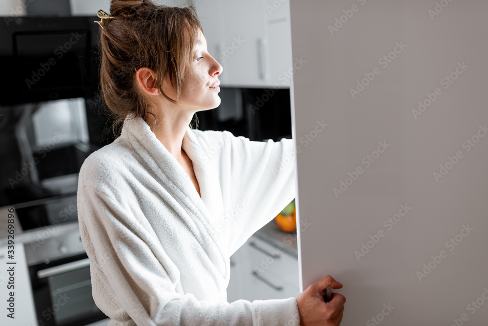 Young woman in bathrobe getting some food from the fridge, feeling hungry at night. Concept of not r