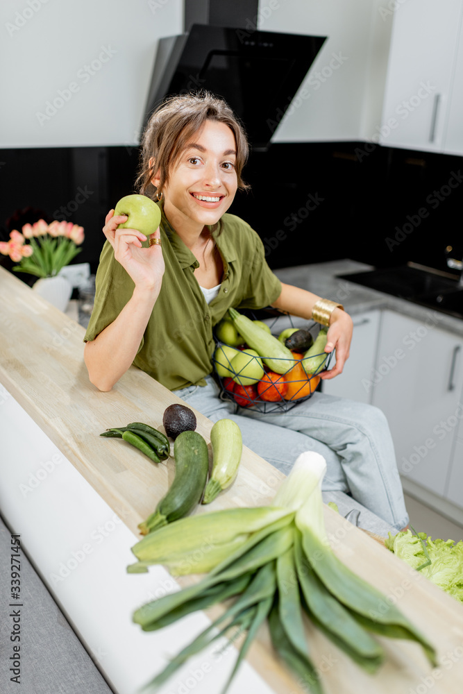 Portrait of a young and cheerful woman with healthy raw food on the kitchen at home. Vegetarianism, 