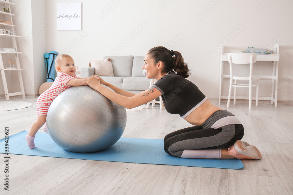 Young sporty mother and her baby doing exercises with fitball at home