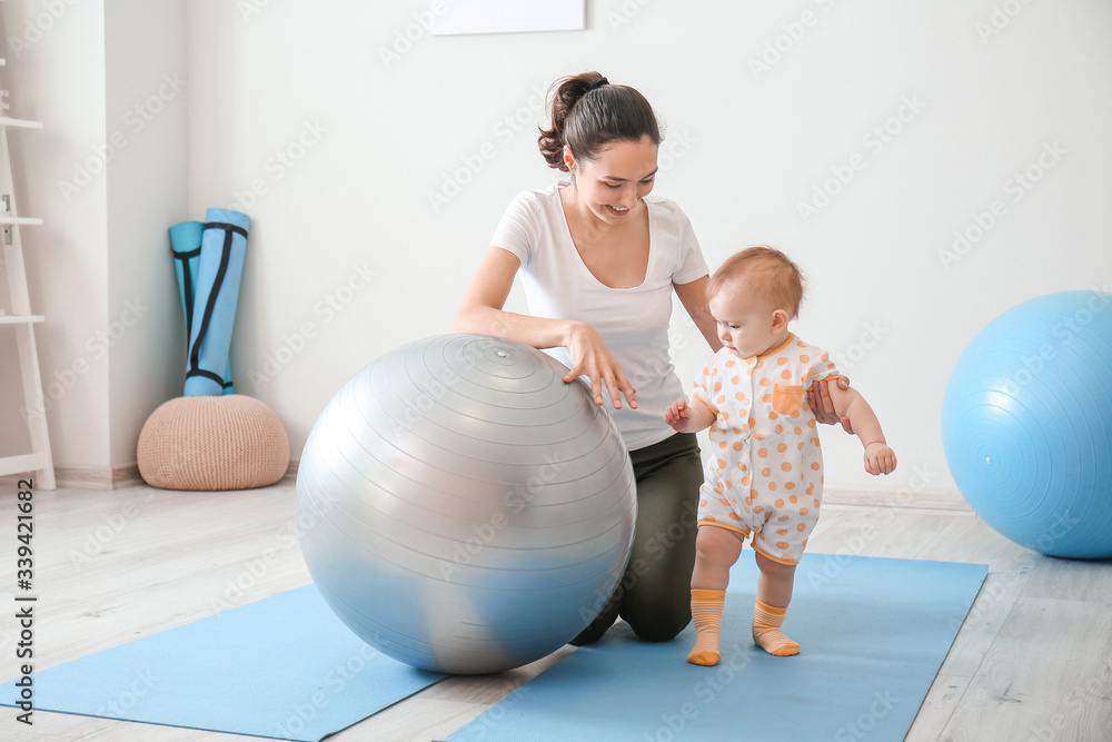 Young sporty mother and her baby doing exercises with fitball at home