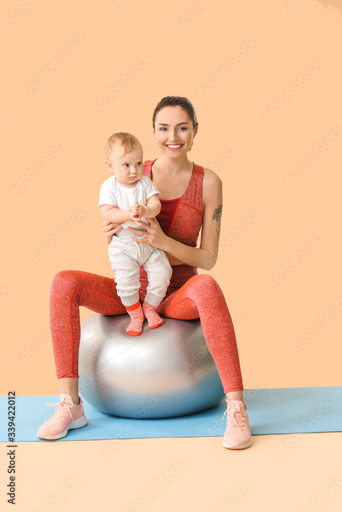 Young sporty mother and her baby doing exercises with fitball on color background