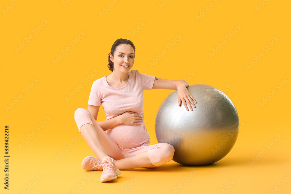 Young pregnant woman doing exercises with fitball on color background