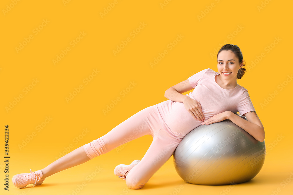 Young pregnant woman doing exercises with fitball on color background