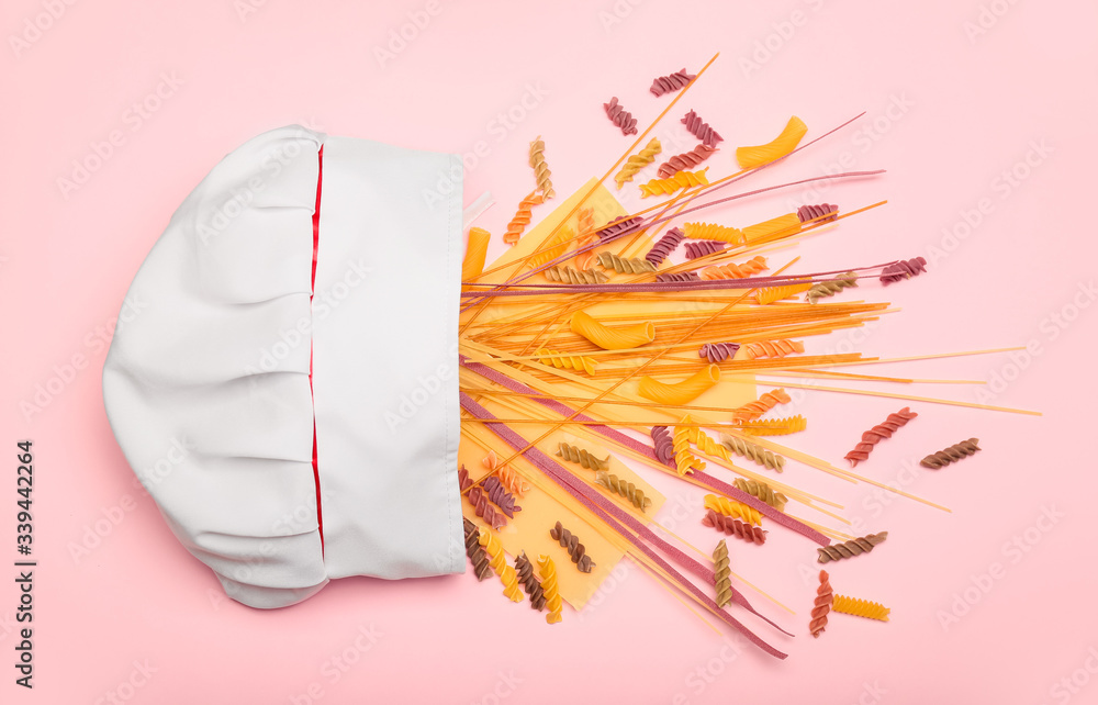 Composition with chefs hat and raw pasta on color background