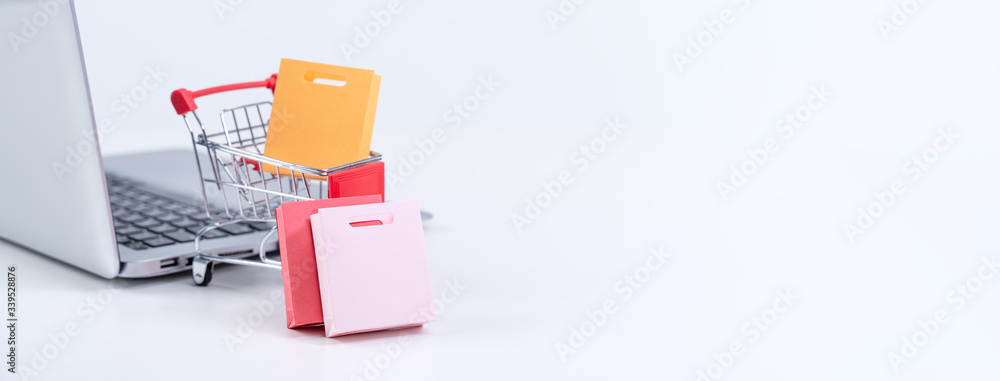 Online shopping. Mini shop cart trolley with colorful paper bags over a laptop computer on white tab