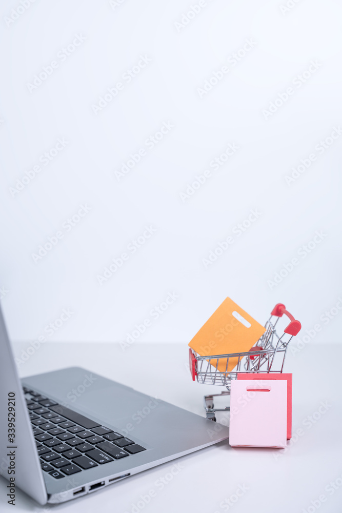 Online shopping. Mini shop cart trolley with colorful paper bags over a laptop computer on white tab