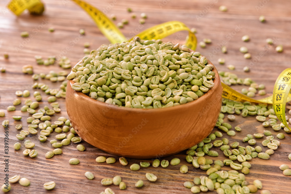 Bowl with green coffee beans and measuring tape on table