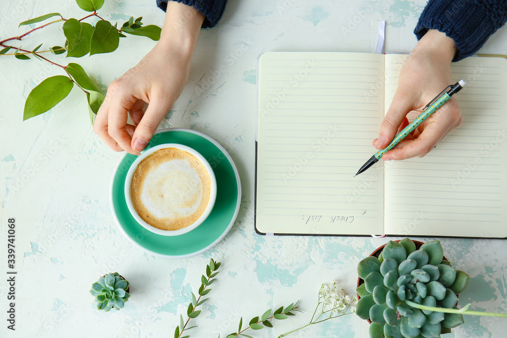 Woman writing in notebook and drinking coffee at table, top view