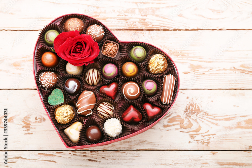 Heart-shaped box with delicious candies on wooden background