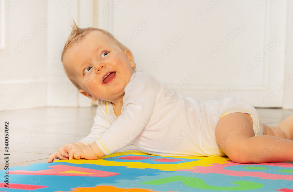 Portrait of laughing happy face of toddler baby boy laying on the floor in nursery room looking back