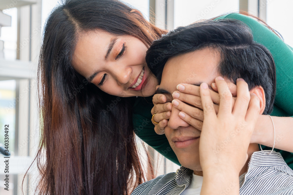 Happy Asian couple play covering eyes in living room.