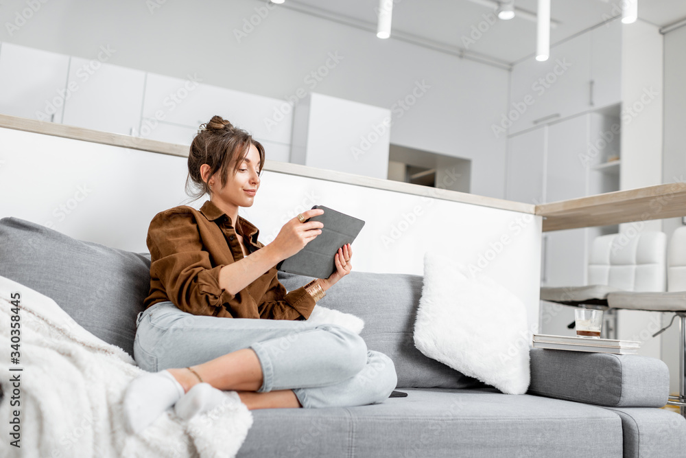 Young relaxed woman working or surfing the internet on a digital tablet while sitting on the couch a