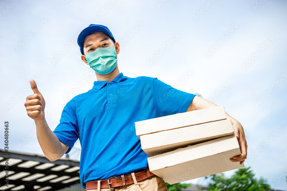 Asian delivery man in blue t-shirt carrying pizza box and showing thumb up. Delivery man concept.