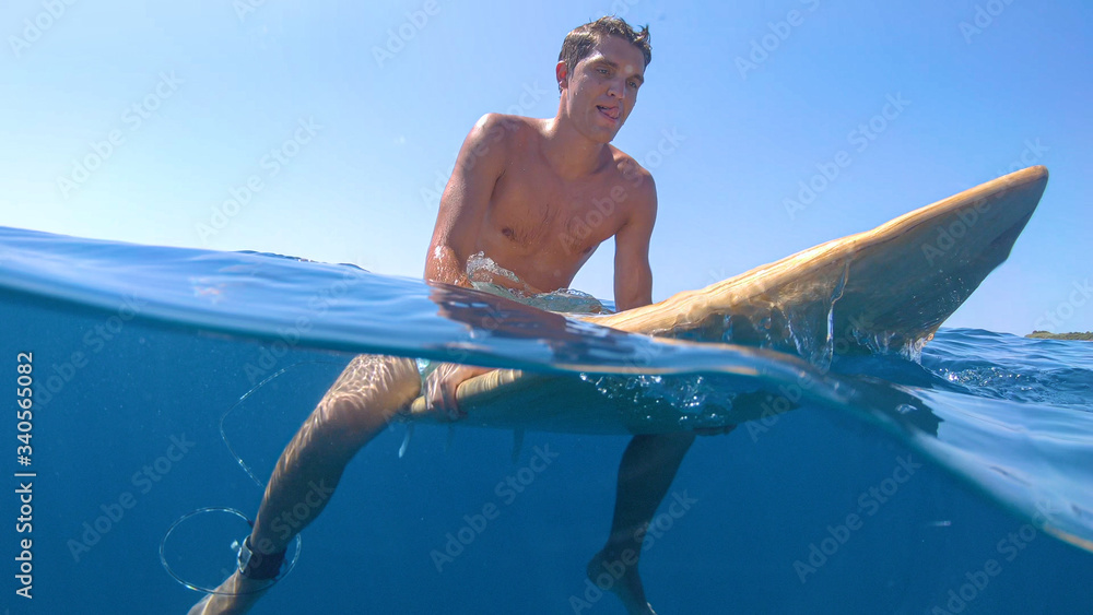 HALF UNDERWATER: Fit young man sits on his surfboard and waits for big waves.