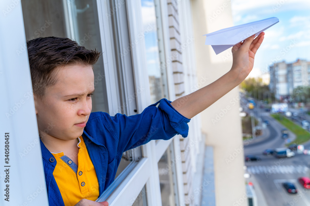 Boy launches paper airplane through the window. Boy forced to stay at home during pandemia. Having f