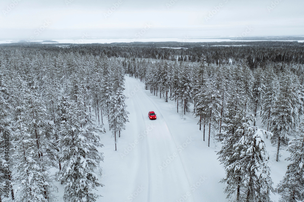 Drone view of a red car driving though a snowy forest in Lapland, Finland