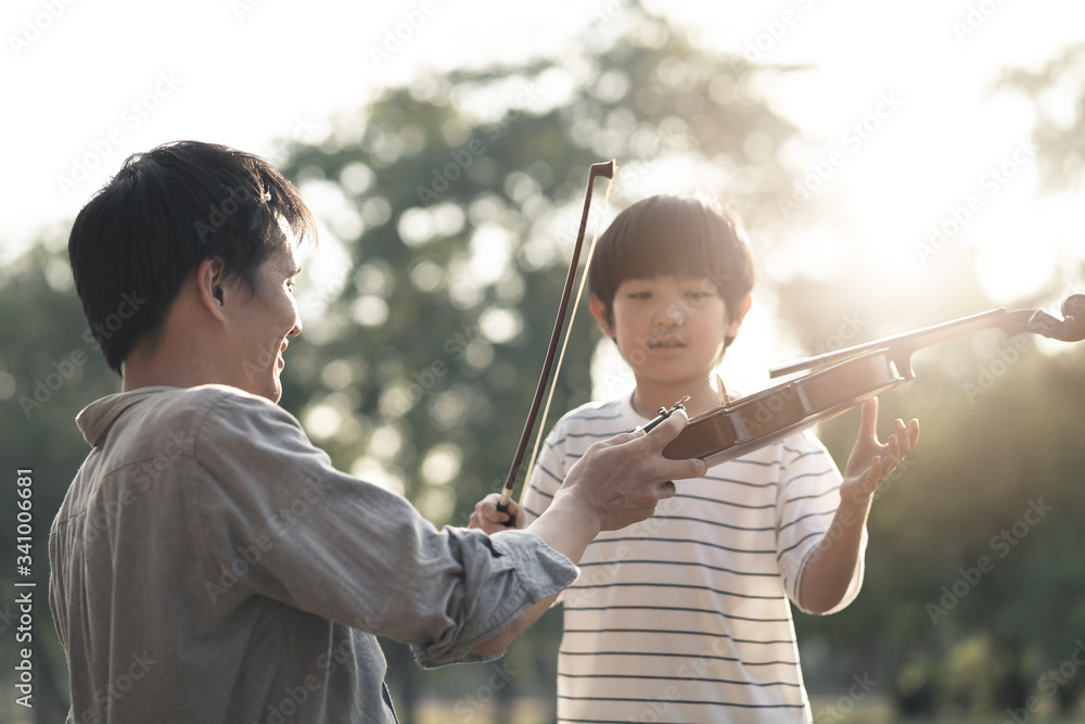 Asian father give and teach young boy kid to play violin in park together. Man educate music skill t