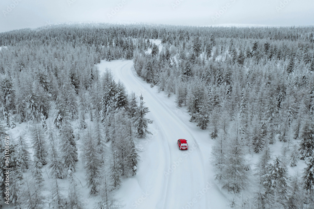 芬兰拉普兰一辆红色汽车在雪地森林中行驶的无人机视图