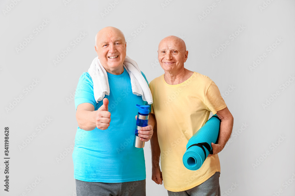 Sporty elderly men with yoga mat and bottle of water on light background