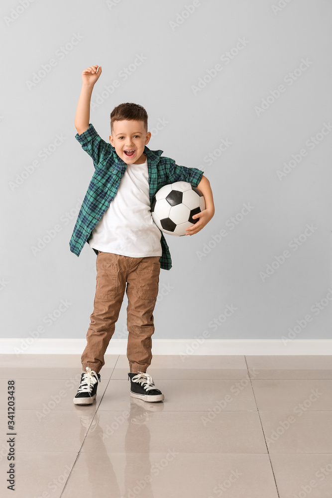 Happy little boy with soccer ball near grey wall