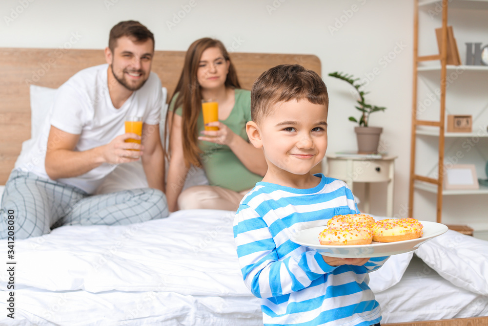 Little boy with pastry for his parents in bedroom