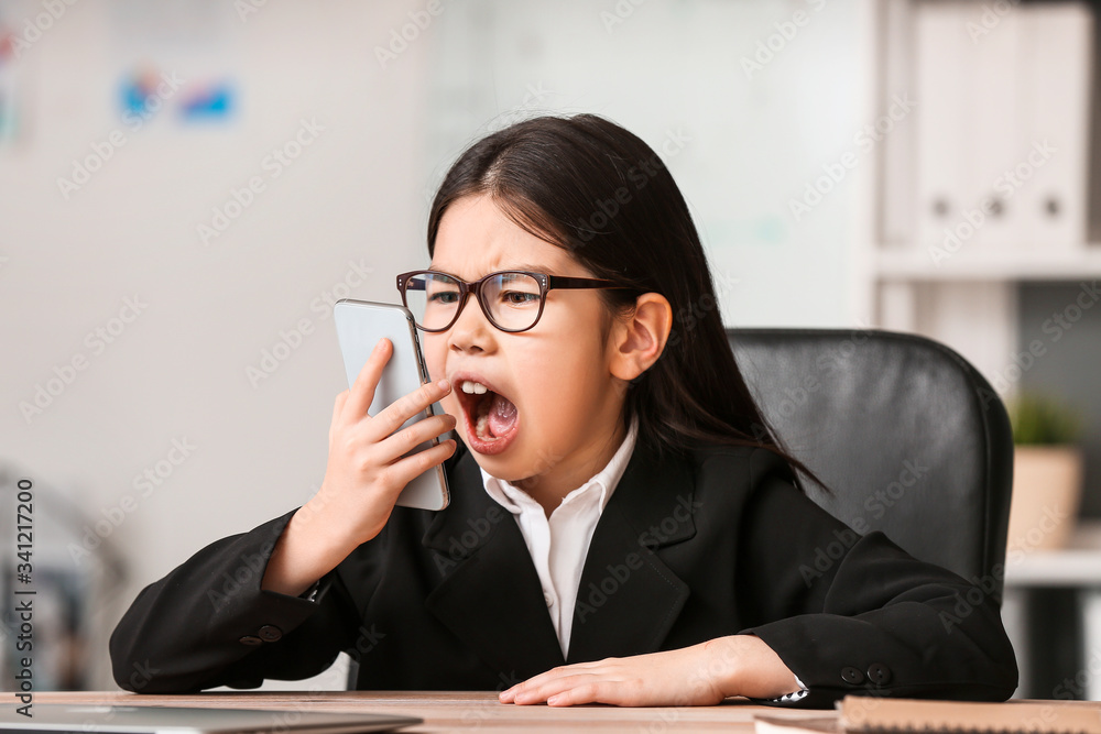 Angry little businesswoman talking by mobile phone in office