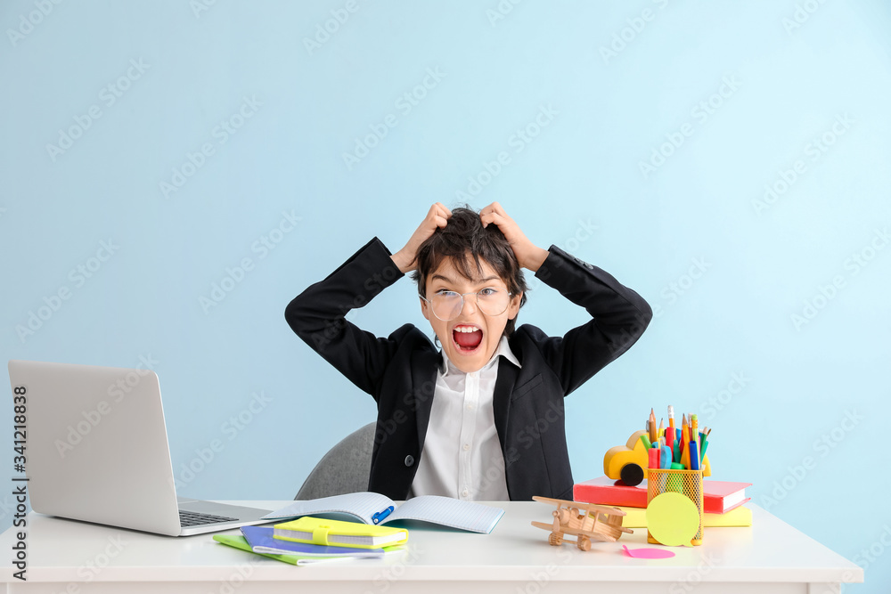 Stressed little boy doing homework against color background